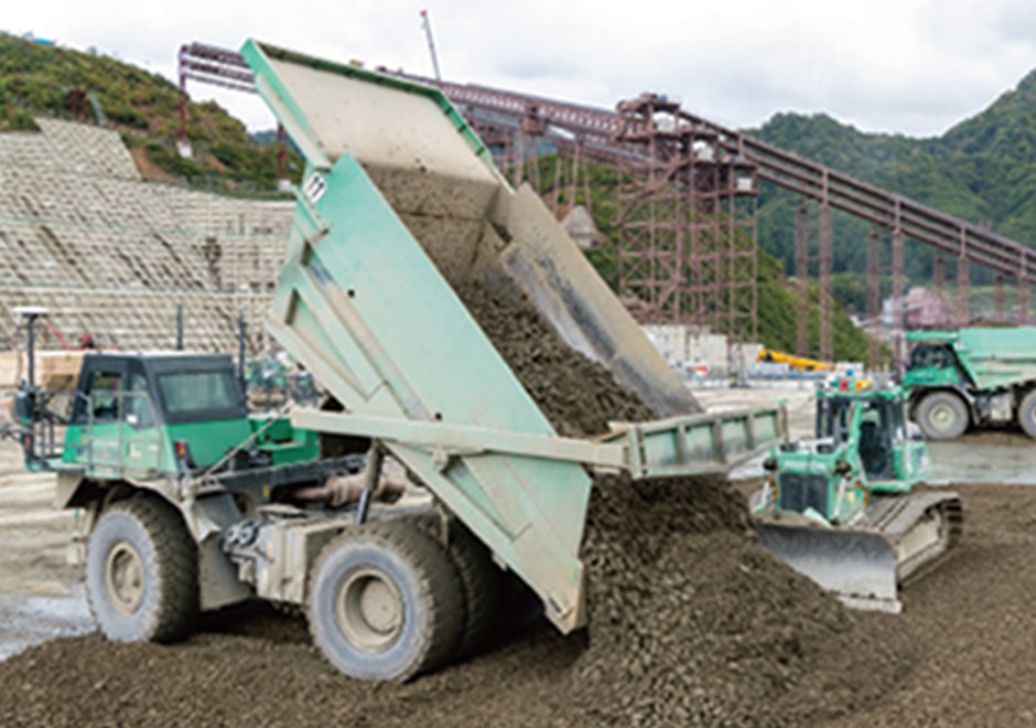 Automated bulldozer waiting while dump truck unloads CSG