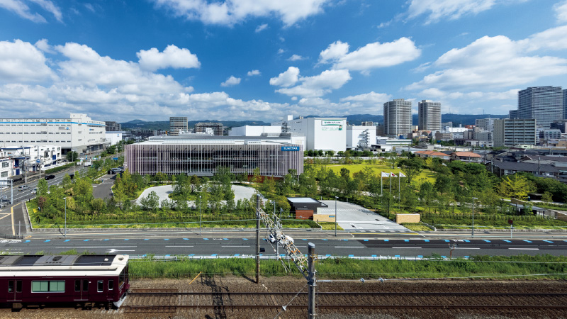 図版:阪急京都線沿いに正対した南東の構え。芝生広場や緑溢れるウォーキングコースなど公園のように地域にひらかれた「コミュニケーションパーク」