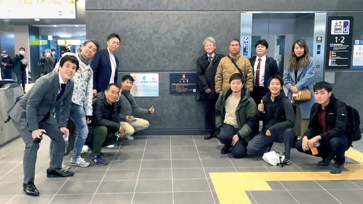 図版:メイン改札口付近の壁面に掲示されている第3回日建連土木賞のブロンズパネルの前で記念撮影