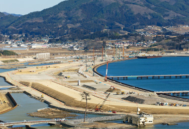 図版:海上輸送で資材を調達するための荷揚げ用仮設桟橋2基(のちに撤去)と海側の第1線提の根固め工がほぼ完成した様子(2015年2月)