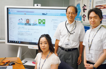 図版:「Ywai!」の画面をバックにする横浜支店管理部総務グループ(情報システム担当)のメンバー