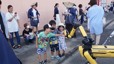 図版：沿道の子どもたちに挨拶をするSpot